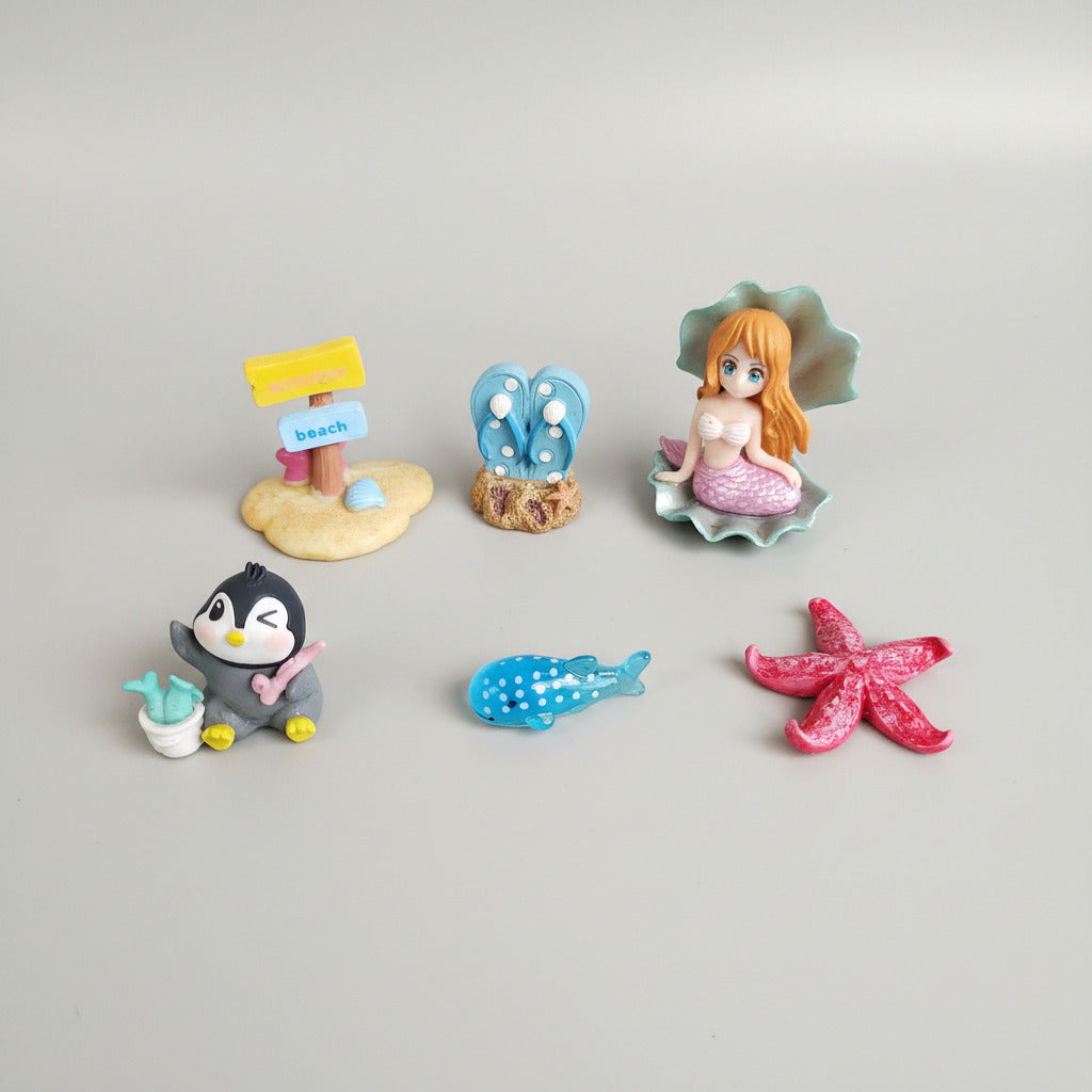 Set of small figurines including a penguin, mermaid, butterfly, and starfish on a textured surface.