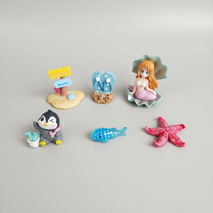 Set of small figurines including a penguin, mermaid, butterfly, and starfish on a textured surface.