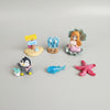Set of small figurines including a penguin, mermaid, butterfly, and starfish on a textured surface.