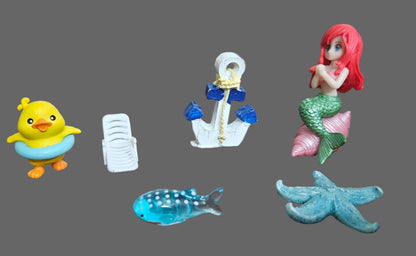 Set of small figurines including a duck, anchor, mermaid, whale, and starfish on a wooden surface.