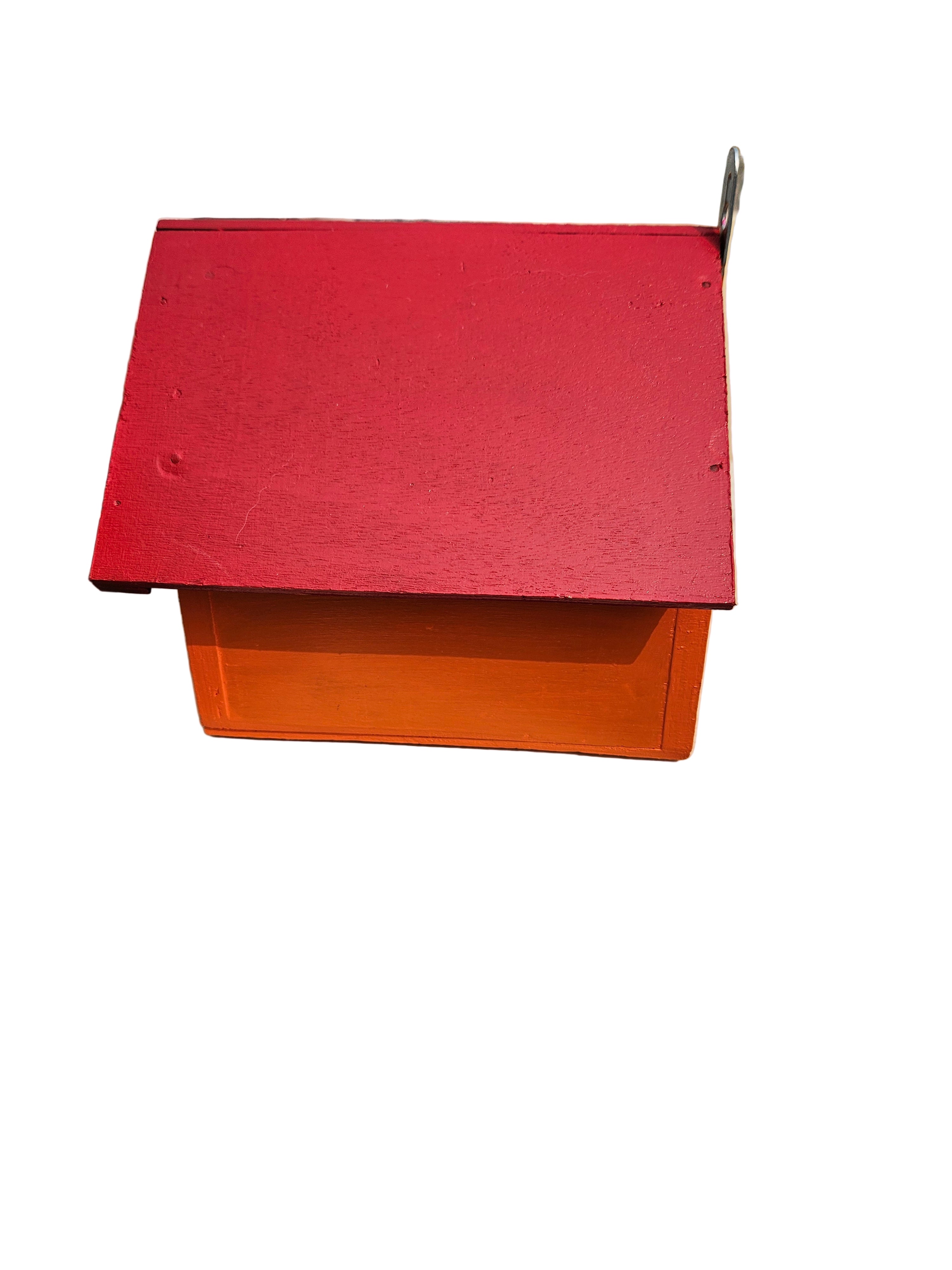 Bird house Red and orange rectangular object on a concrete surface with buildings in the background 