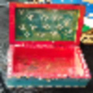 A small hand-painted wooden box with an open lid, featuring a red exterior, a teal interior, and white floral designs painted on the inside of the lid.
